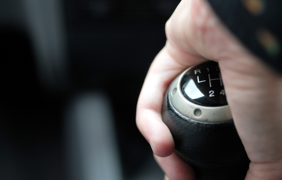 De hand van een persoon op de versnellingspook van een handgeschakelde auto, symboliseert de controle die nodig is bij rijlessen voor ADHD.