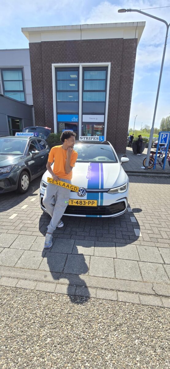 Leerling leunt trots tegen de Volkswagen Golf na het behalen van het rijbewijs
