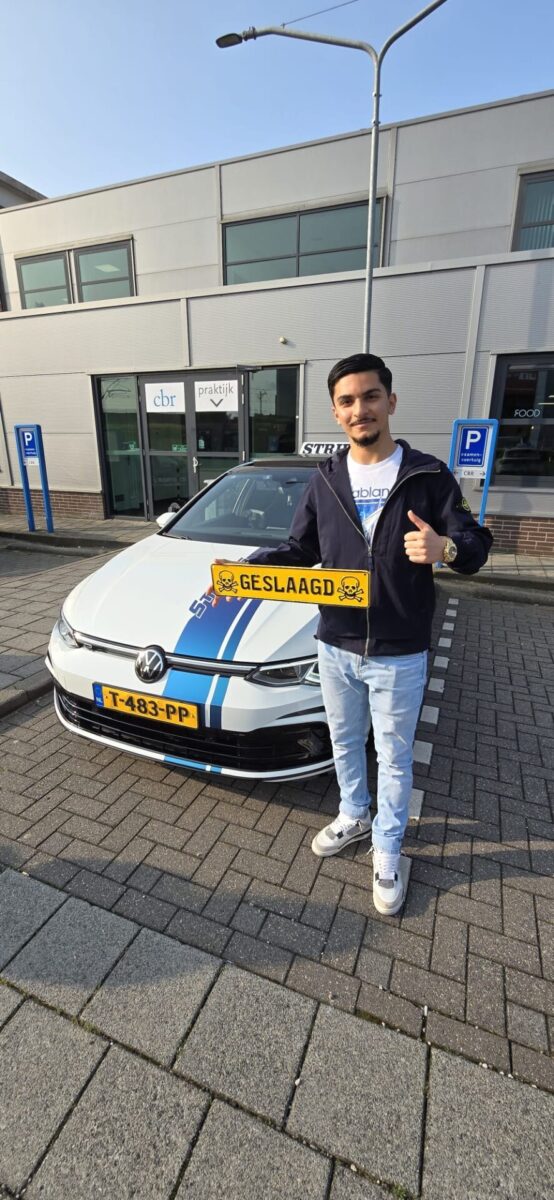 Leerling steekt duim omhoog met geslaagd-bord bij de schakelauto in Rotterdam