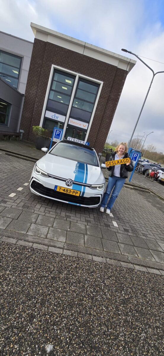 Leerling met geslaagd-bord naast de gestreepte schakelauto van Rijschool Stripes