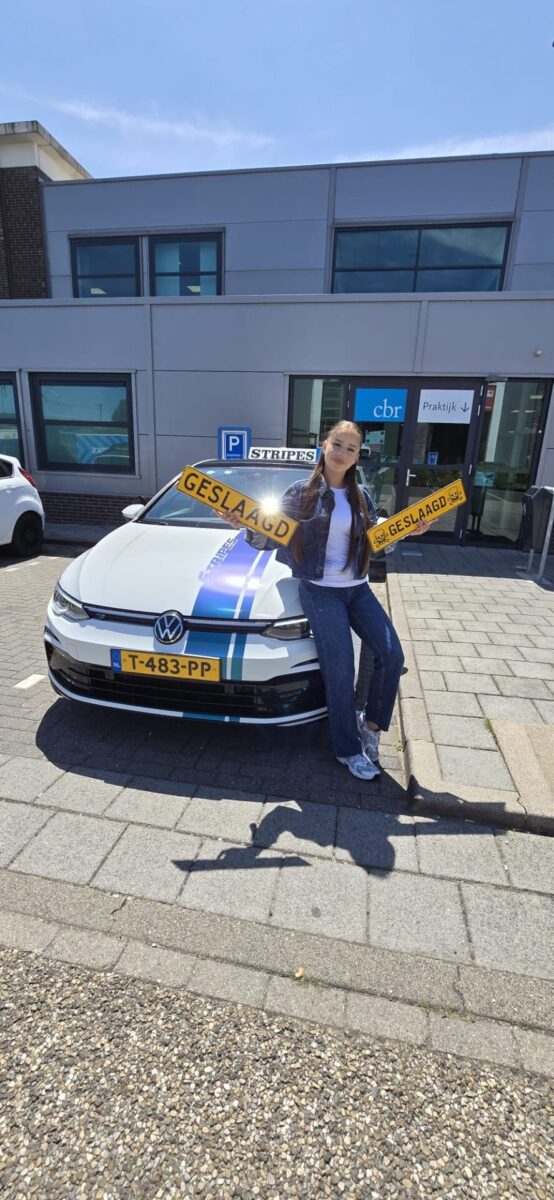 Leerling houdt twee geslaagd-borden omhoog bij de Volkswagen Golf lesauto