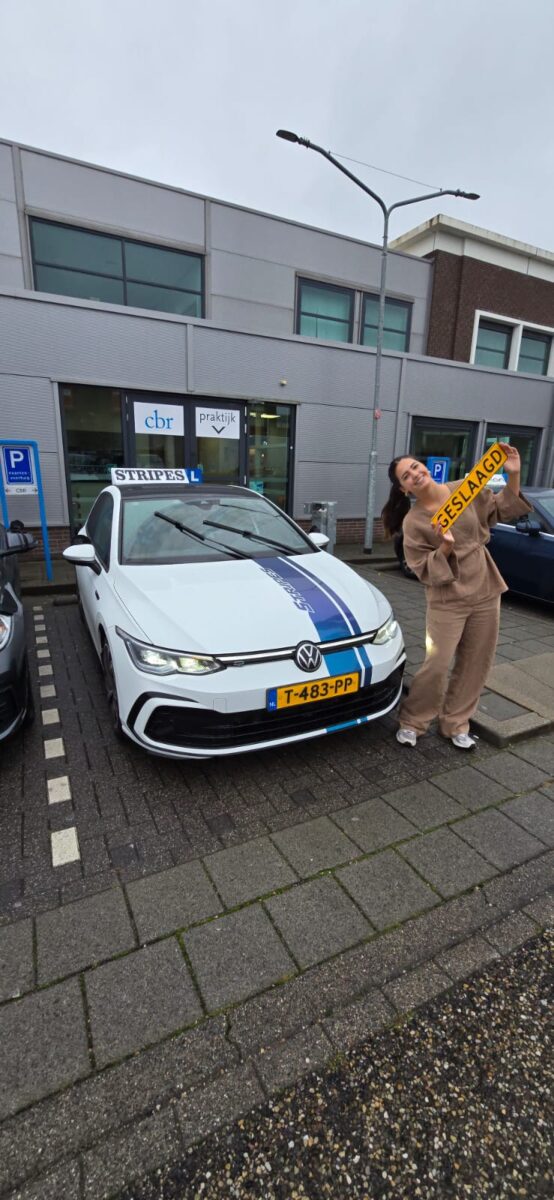 Leerling toont het geslaagd-bord naast de schakelauto van Rijschool Stripes