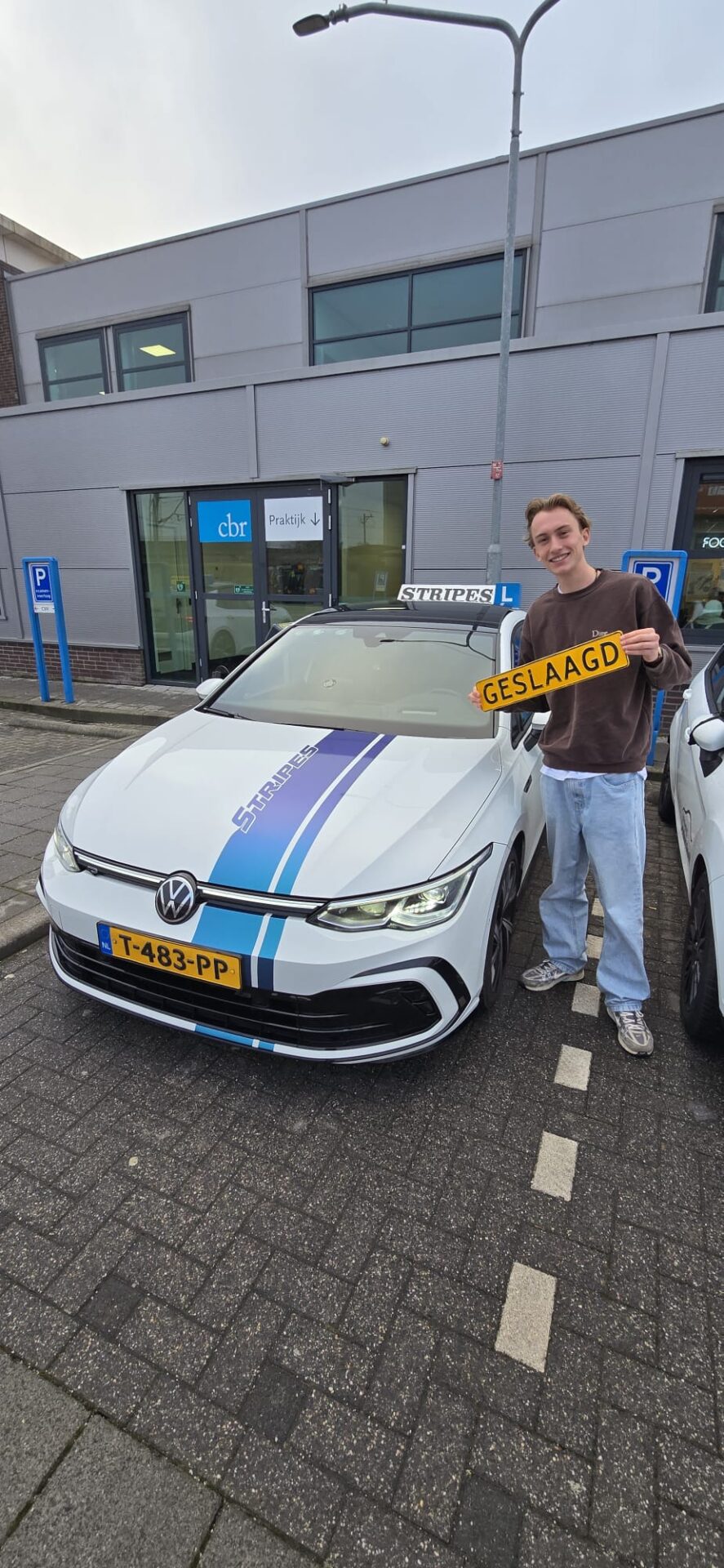 Geslaagde leerling van Rijschool Stripes poseert trots bij de lesauto