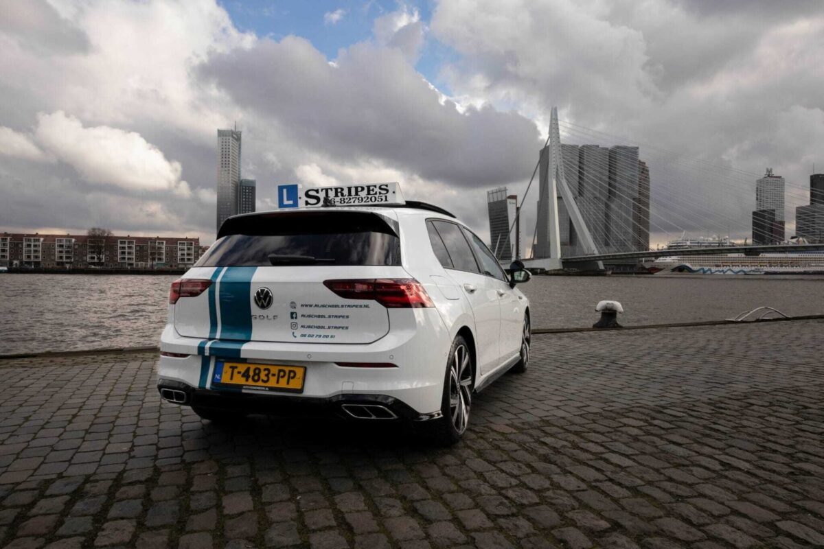 Schakel lesauto van Rijschool Stripes bij de Erasmusbrug, achteraanzicht met contactgegevens op het dak